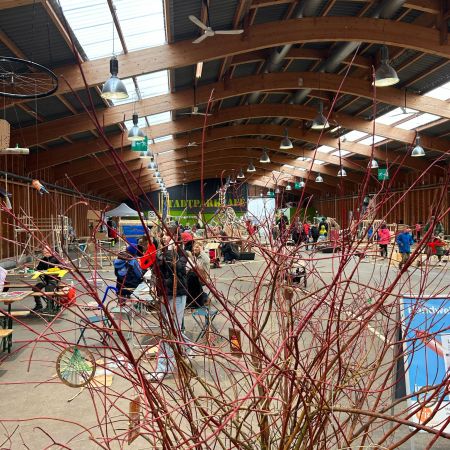 Blick in eine grosse Halle voller Menschen, im Vordergrund hat es eine Pflanze.